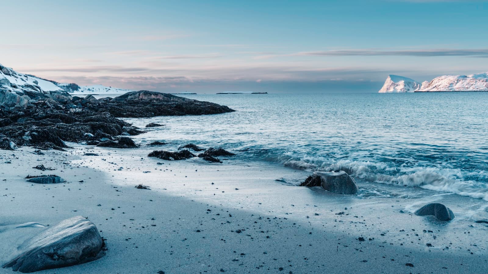 Waves on a snow-dusted Arctic beach, with low mountains across the water