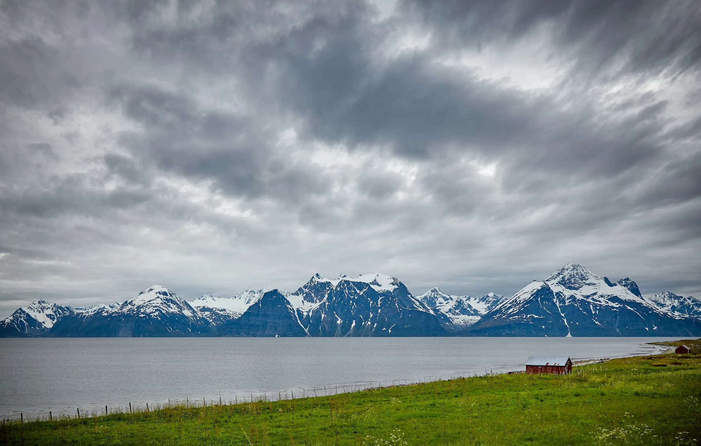 The snow-capped Lyngen Alps across a grey fjord under heavy cloud